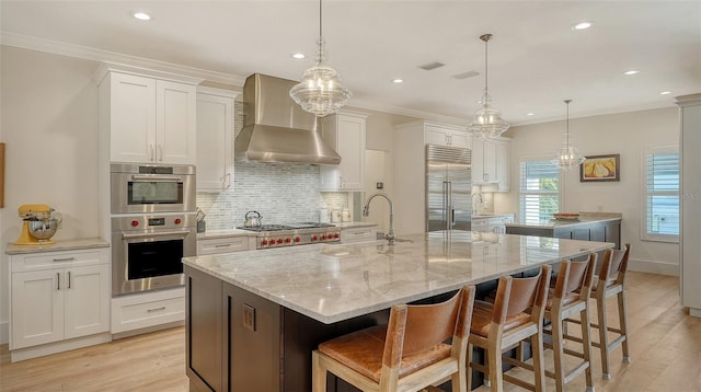 kitchen featuring a spacious island, wall chimney exhaust hood, white cabinetry, appliances with stainless steel finishes, and pendant lighting