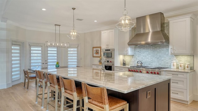 kitchen with a spacious island, wall chimney exhaust hood, white cabinetry, tasteful backsplash, and stainless steel appliances