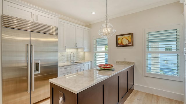 kitchen with white cabinetry, sink, hanging light fixtures, and stainless steel built in fridge