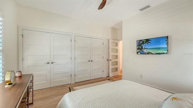 bedroom featuring ceiling fan, light hardwood / wood-style floors, and two closets