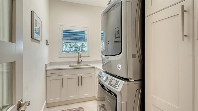 clothes washing area featuring stacked washer / dryer, sink, light tile patterned floors, and cabinets