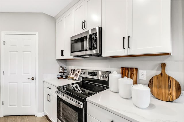 kitchen featuring light stone countertops, white cabinetry, appliances with stainless steel finishes, and light hardwood / wood-style floors