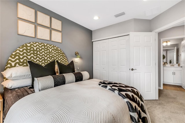 bedroom featuring ensuite bathroom, sink, light colored carpet, and a closet