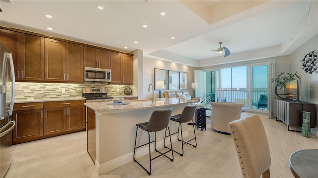 kitchen with appliances with stainless steel finishes, a kitchen breakfast bar, light stone counters, an island with sink, and decorative backsplash