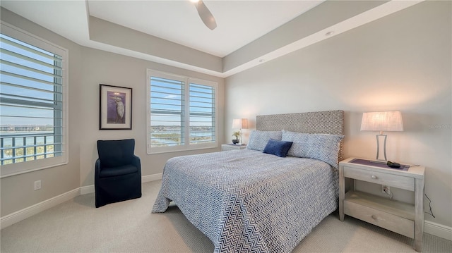 carpeted bedroom with ceiling fan and a tray ceiling