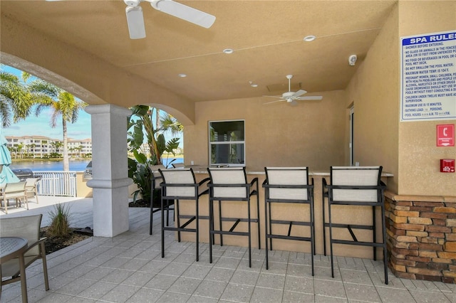 view of patio / terrace with a water view, ceiling fan, and an outdoor bar