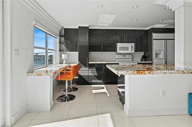 kitchen with built in desk, light tile patterned floors, white appliances, light stone countertops, and decorative backsplash