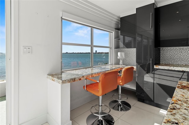 bar featuring light tile patterned flooring, built in desk, tasteful backsplash, light stone countertops, and a water view