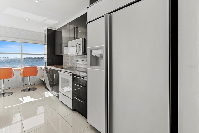 kitchen with white appliances, light tile patterned flooring, decorative backsplash, and a water view