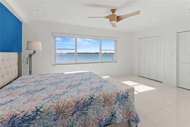 tiled bedroom with a water view, ceiling fan, and two closets