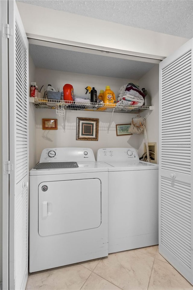 laundry area featuring separate washer and dryer, light tile patterned floors, and a textured ceiling