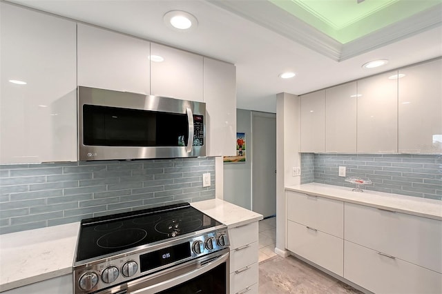 kitchen with white cabinetry, ornamental molding, appliances with stainless steel finishes, light stone countertops, and decorative backsplash