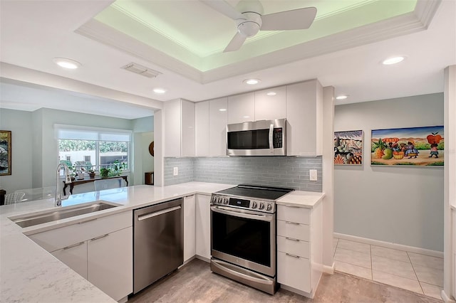 kitchen with sink, a tray ceiling, kitchen peninsula, stainless steel appliances, and white cabinets