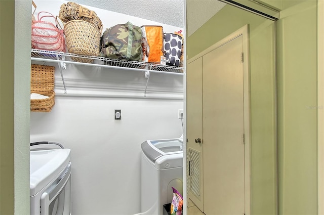 clothes washing area with washing machine and dryer and a textured ceiling