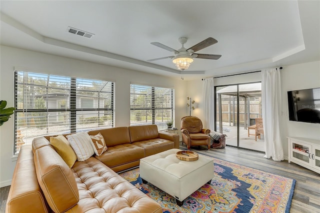 living room featuring ceiling fan, wood-type flooring, a raised ceiling, and plenty of natural light