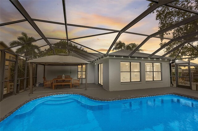 pool at dusk with a lanai and a patio area