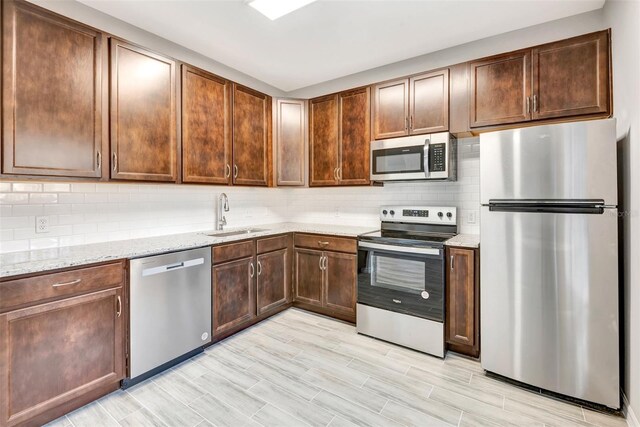 kitchen featuring sink, appliances with stainless steel finishes, light stone countertops, decorative backsplash, and light wood-type flooring