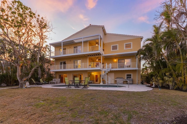 back house at dusk featuring a patio, a balcony, a yard, and ceiling fan