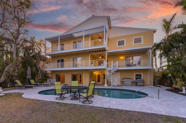 back house at dusk featuring ceiling fan, a balcony, and a patio