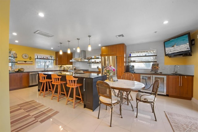 kitchen featuring a kitchen bar, decorative light fixtures, appliances with stainless steel finishes, a kitchen island with sink, and exhaust hood