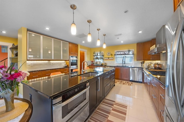 kitchen with stainless steel appliances, sink, a kitchen island with sink, and hanging light fixtures