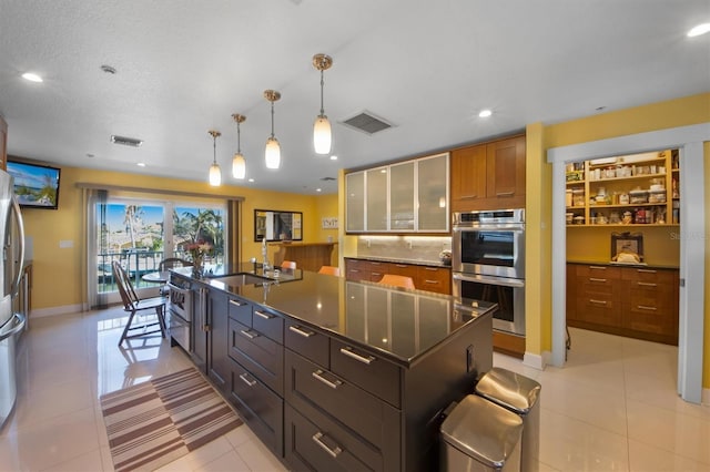 kitchen featuring light tile patterned flooring, sink, hanging light fixtures, stainless steel appliances, and a center island with sink