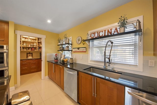 kitchen with appliances with stainless steel finishes, tasteful backsplash, sink, dark stone countertops, and light tile patterned floors