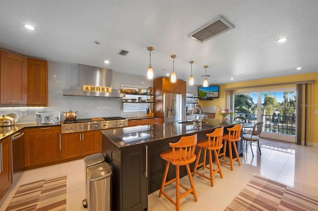 kitchen with extractor fan, light tile patterned floors, appliances with stainless steel finishes, a kitchen breakfast bar, and an island with sink