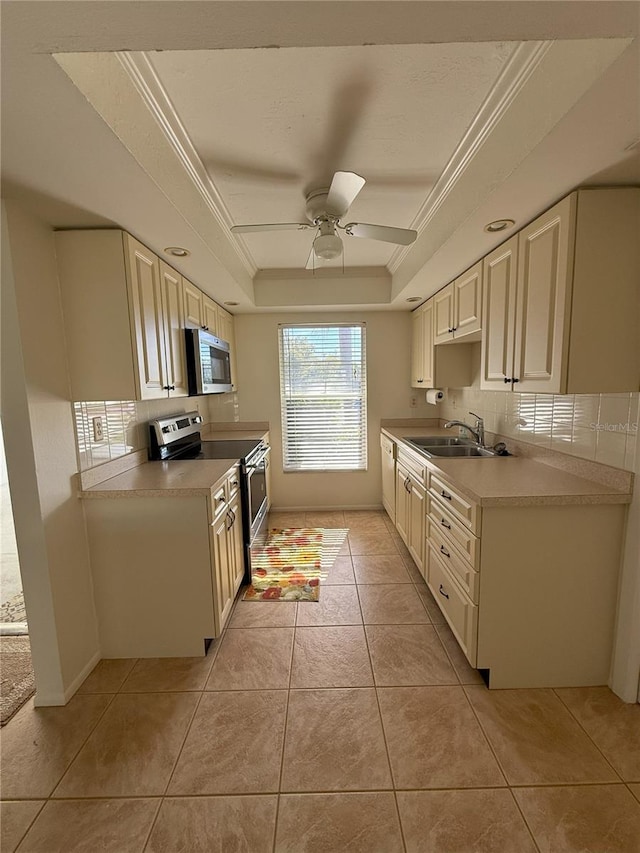 kitchen with sink, light tile patterned floors, appliances with stainless steel finishes, cream cabinets, and a tray ceiling