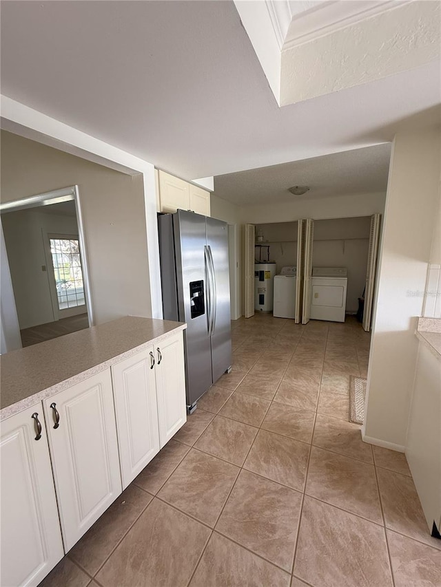 kitchen featuring stainless steel refrigerator with ice dispenser, white cabinetry, washer / dryer, and electric water heater