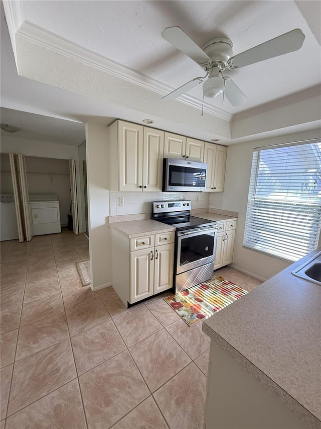 kitchen featuring light tile patterned flooring, a raised ceiling, washer / clothes dryer, stainless steel appliances, and cream cabinets