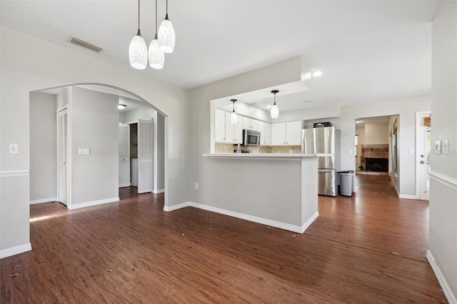 kitchen with appliances with stainless steel finishes, white cabinets, decorative backsplash, kitchen peninsula, and dark wood-type flooring