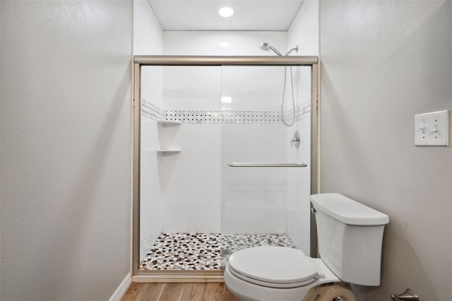 bathroom with wood-type flooring, a shower with shower door, and toilet