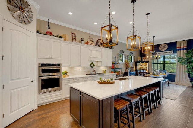 kitchen with white cabinetry, appliances with stainless steel finishes, pendant lighting, and a center island with sink