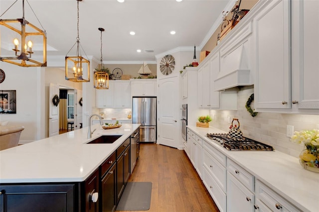 kitchen featuring a kitchen island with sink, sink, decorative light fixtures, and appliances with stainless steel finishes