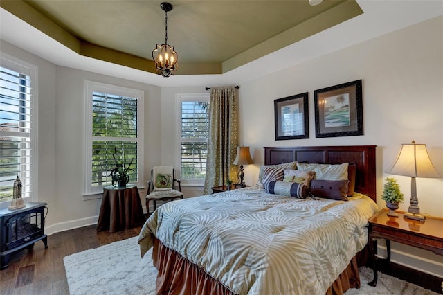 bedroom featuring dark hardwood / wood-style floors, a raised ceiling, and a chandelier