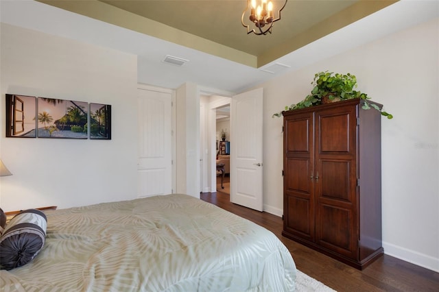 bedroom featuring dark wood-type flooring, a tray ceiling, and a chandelier