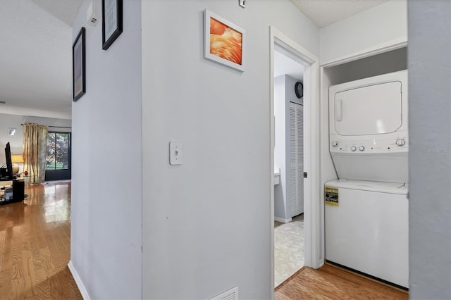 clothes washing area with stacked washer / drying machine, a textured ceiling, and light wood-type flooring