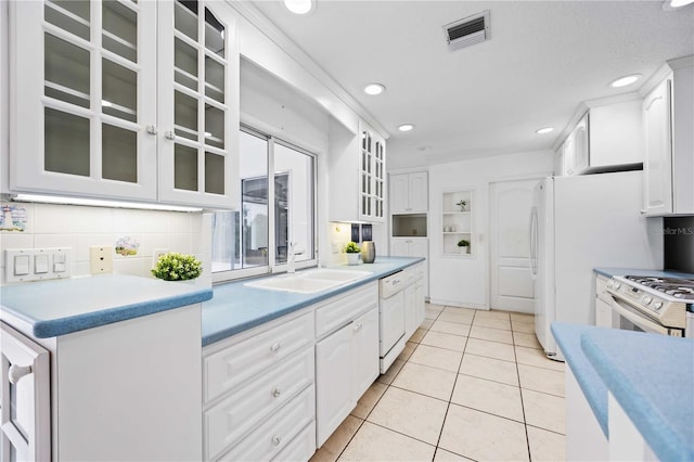 kitchen with tasteful backsplash, sink, white cabinets, light tile patterned floors, and white appliances