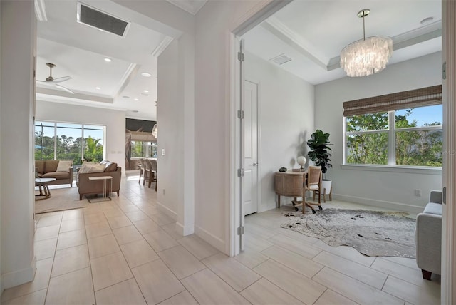 corridor with an inviting chandelier, ornamental molding, and a raised ceiling