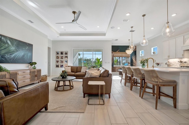 tiled living room featuring a raised ceiling, ornamental molding, sink, and ceiling fan