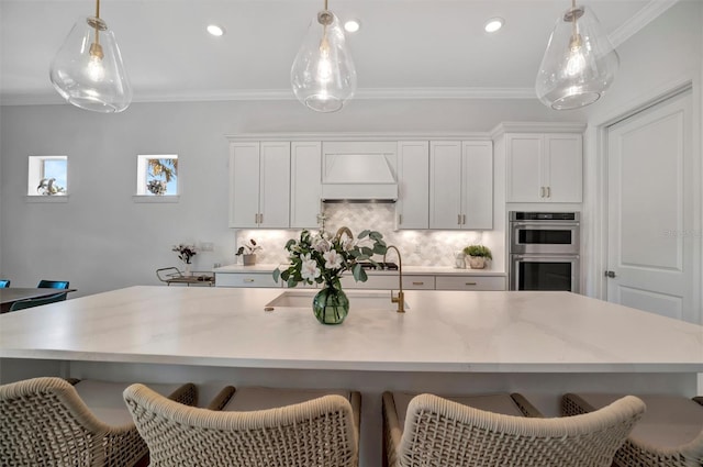 kitchen with decorative light fixtures, double oven, custom range hood, and a center island with sink