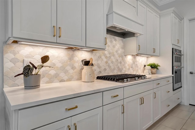 kitchen with light tile patterned floors, premium range hood, stainless steel appliances, tasteful backsplash, and white cabinets