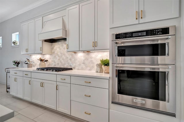 kitchen with premium range hood, white cabinetry, stainless steel appliances, ornamental molding, and decorative backsplash