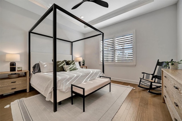 bedroom with ceiling fan, dark hardwood / wood-style flooring, and a tray ceiling