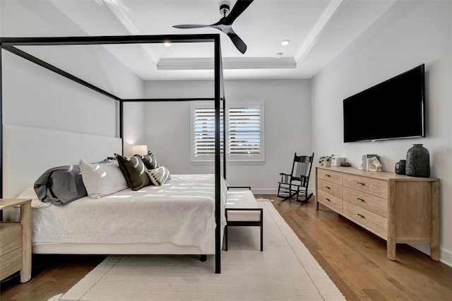 bedroom featuring a tray ceiling, dark wood-type flooring, ornamental molding, and ceiling fan