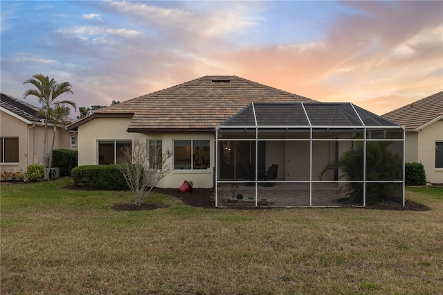 back house at dusk featuring a lanai and a lawn