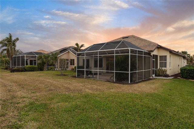 back house at dusk featuring a lanai and a yard