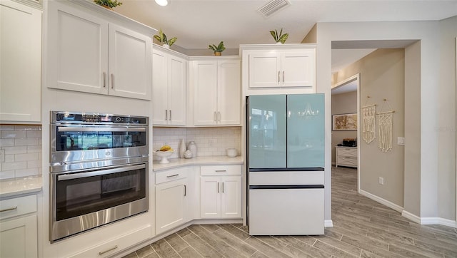 kitchen with white cabinetry, fridge, stainless steel double oven, and backsplash