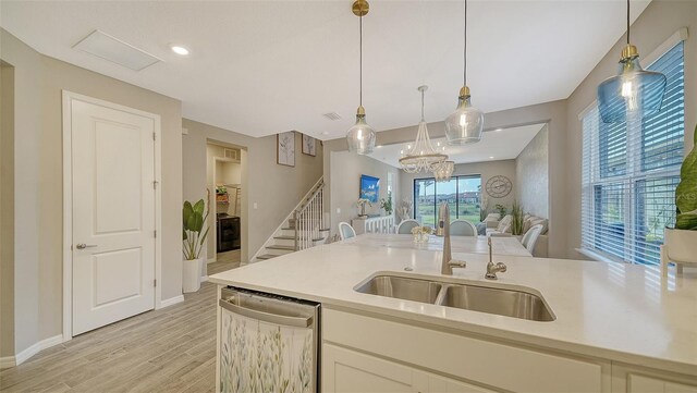 kitchen featuring sink, light hardwood / wood-style flooring, dishwasher, white cabinets, and decorative light fixtures